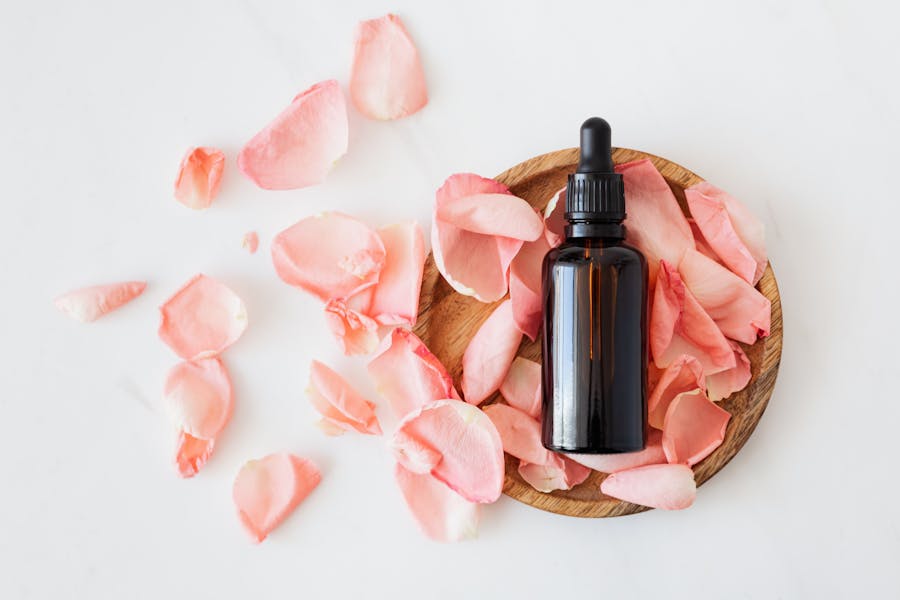 Cosmetic oil bottle with fresh pink rose petals on wooden plate
